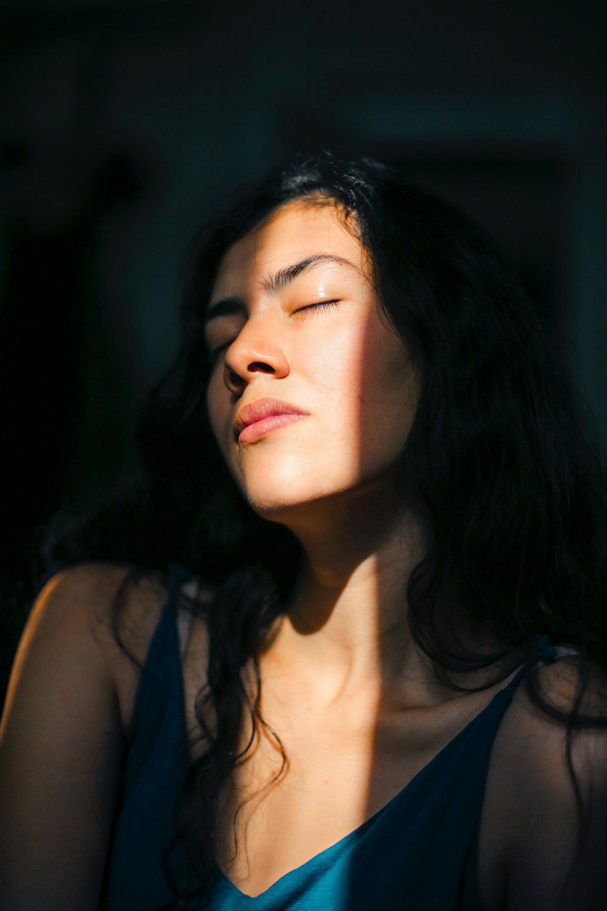 Woman standing in a beam of sunlight, closing her eyes.