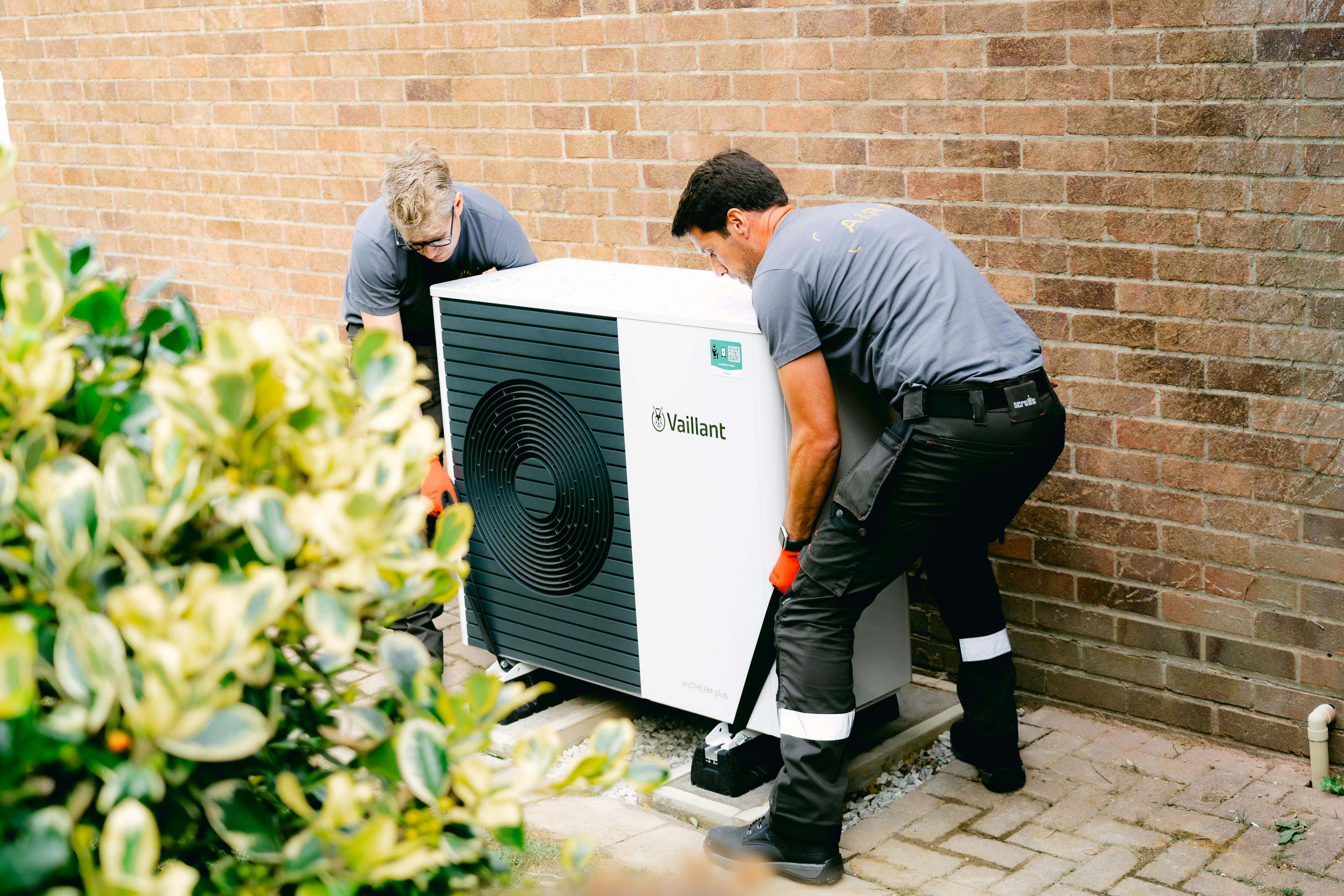 Two Aira Clean Energy Experts putting an air source heat pump outdoor unit onto its base
