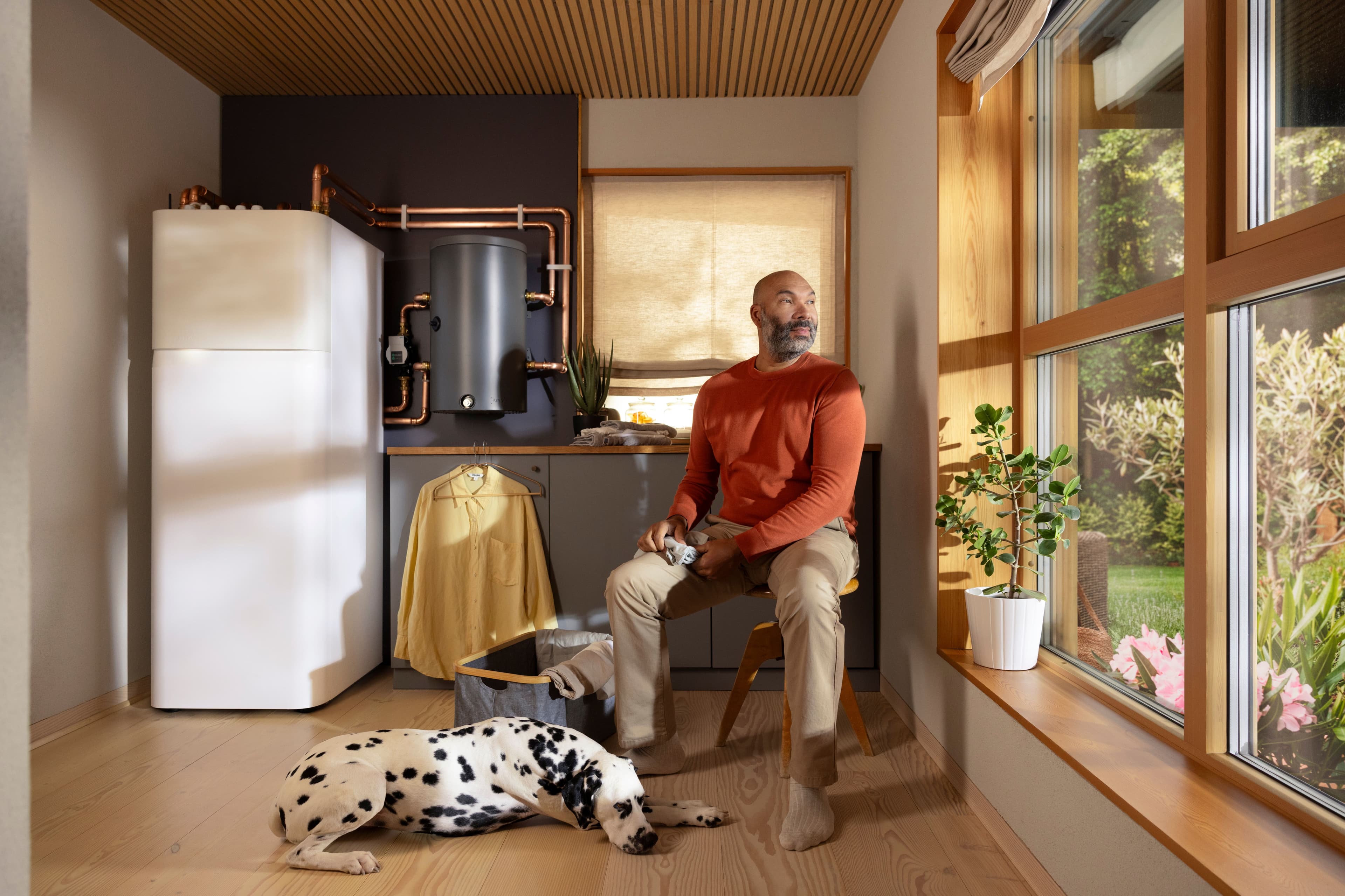 A man is sitting in his laundry room with his dog with an Aira Heat Pump Indoor Unit in the background