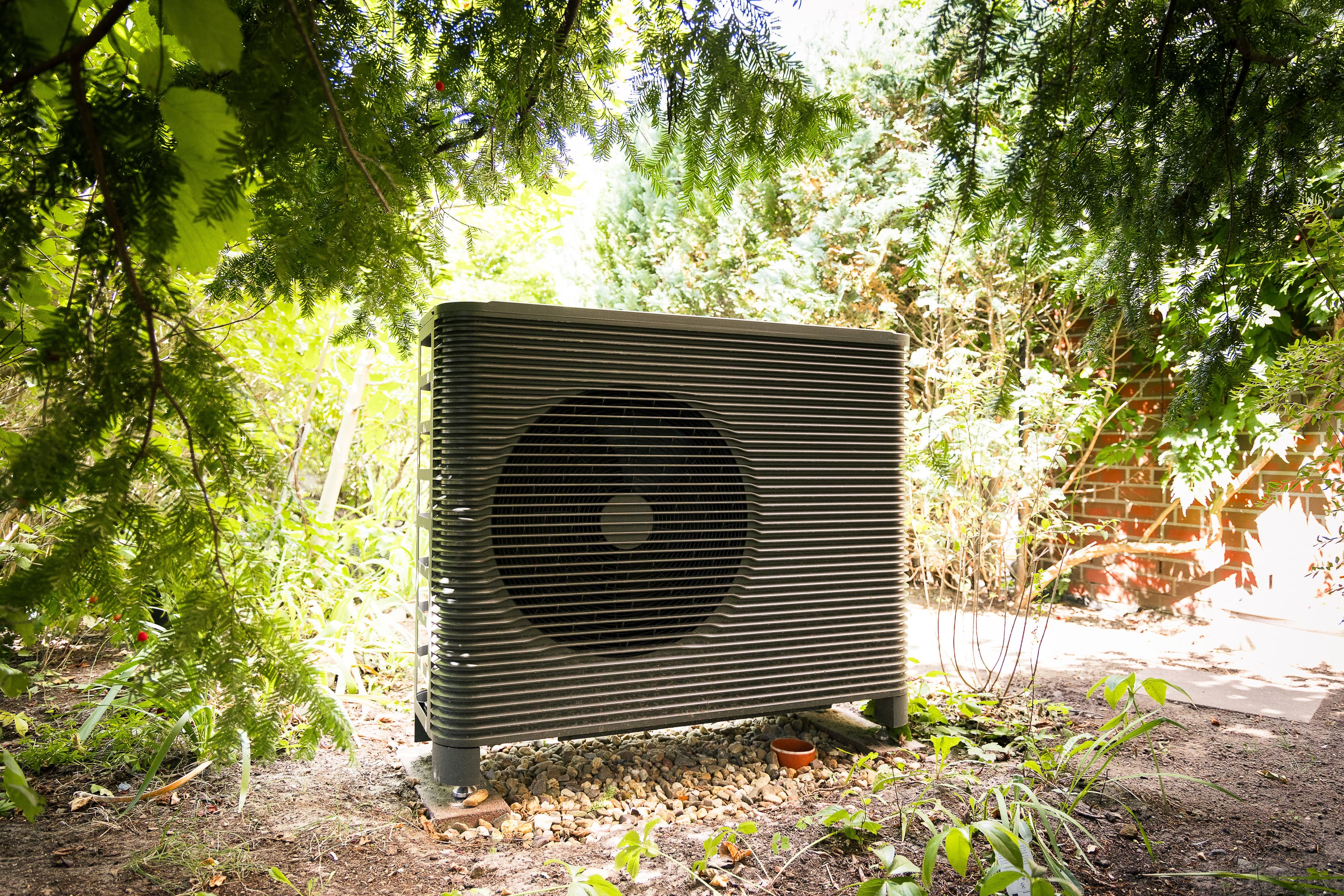 Wärmepumpe steht im Garten und wird von hinten von der Sonne angestrahlt