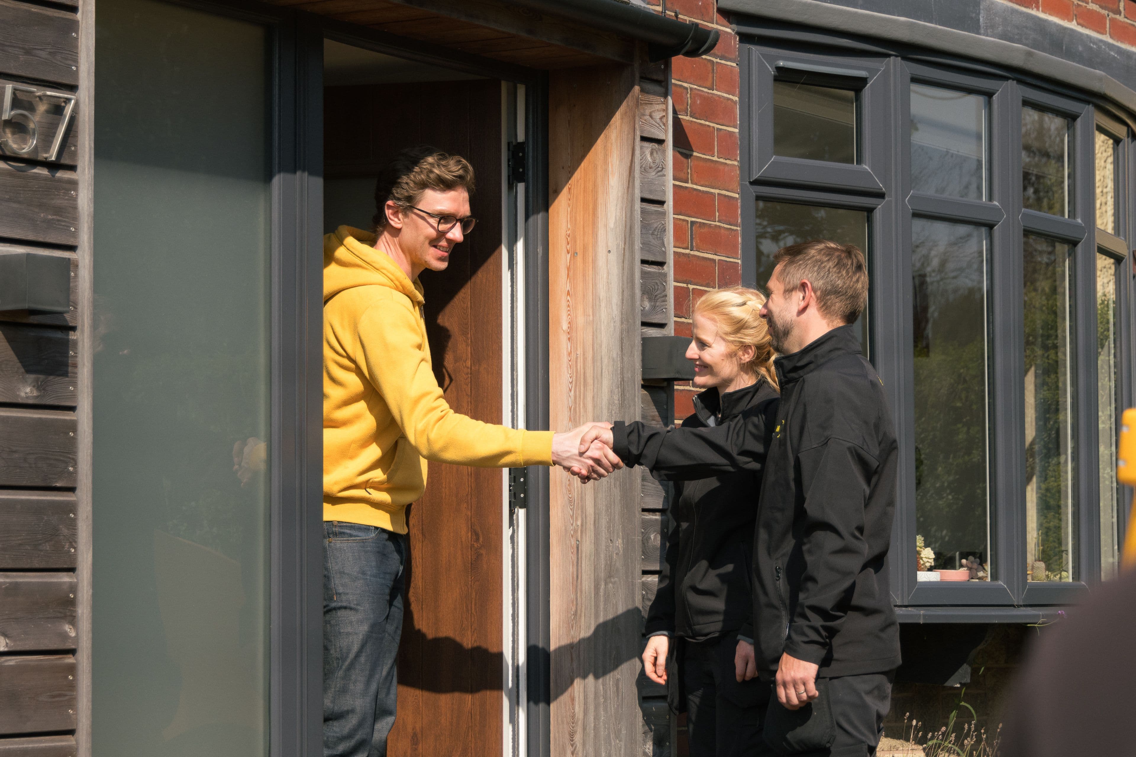Man shaking hands with two Aira Clean Energy Technicians ahead of an Aira Heat Pump installaition at his home