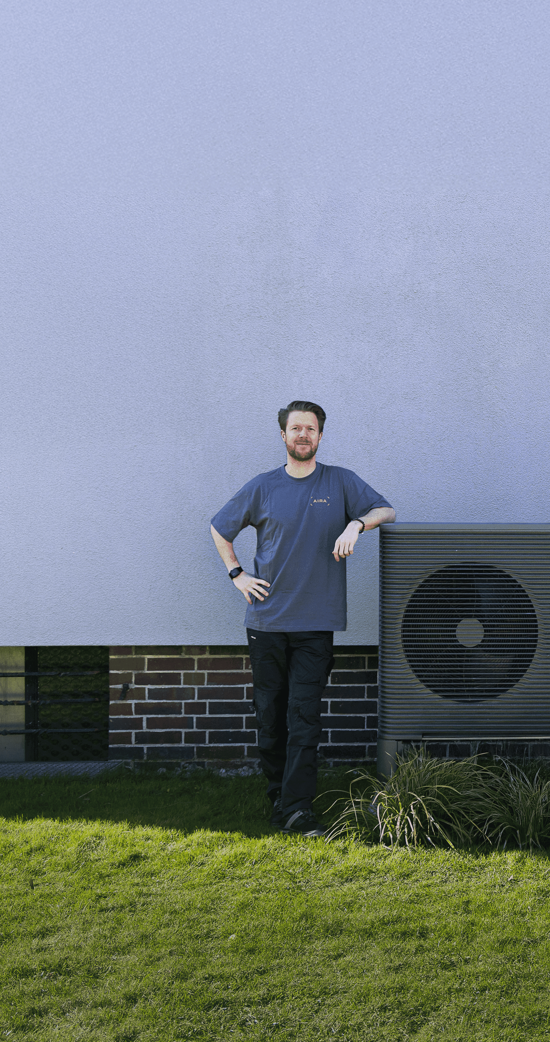 Ein Installateur von Aira steht neben einer Wärmepumpe vor einer weißen Wand im Garten