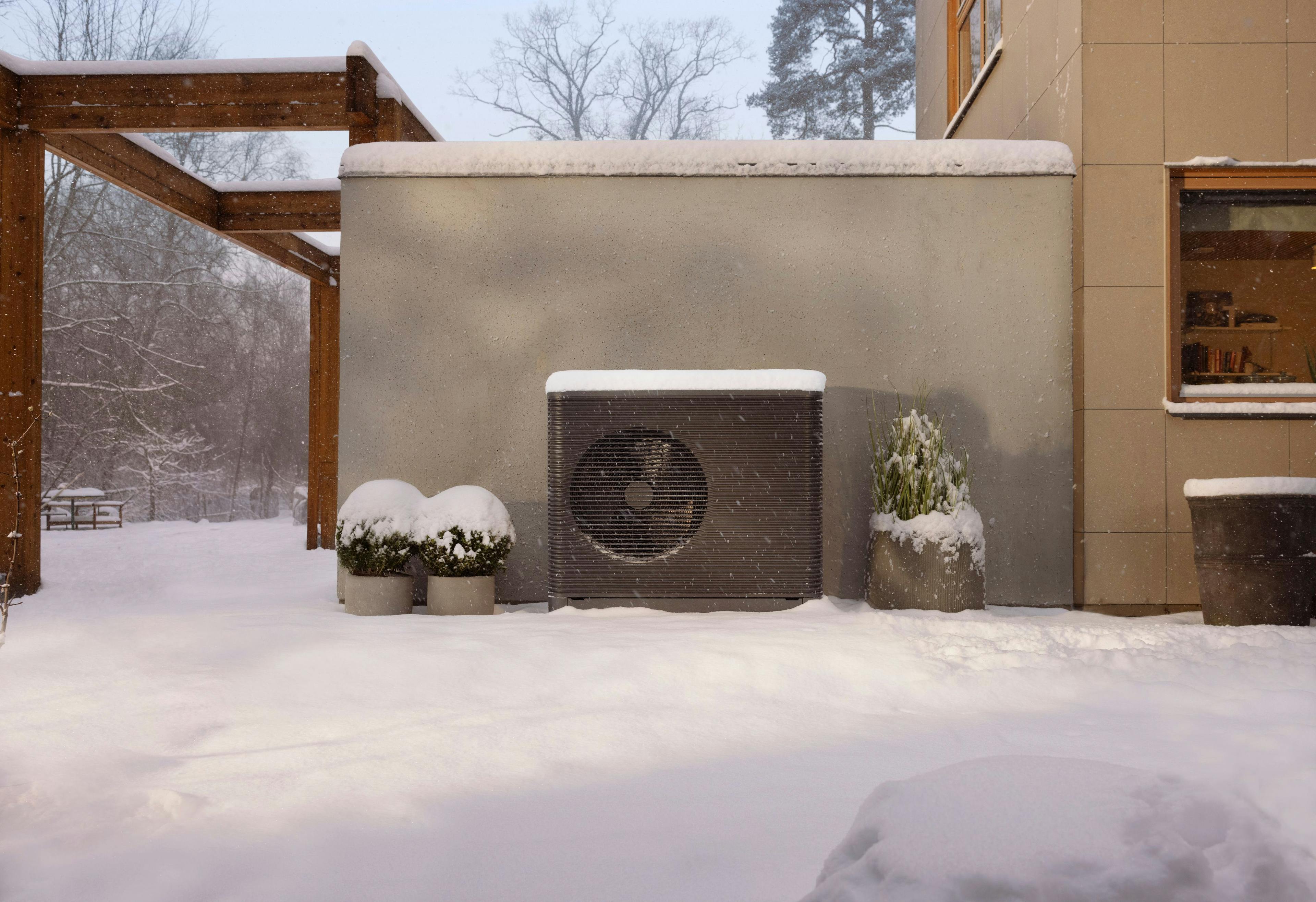 Aira Heat Pump outdoor unit against a grey wall covered in snow