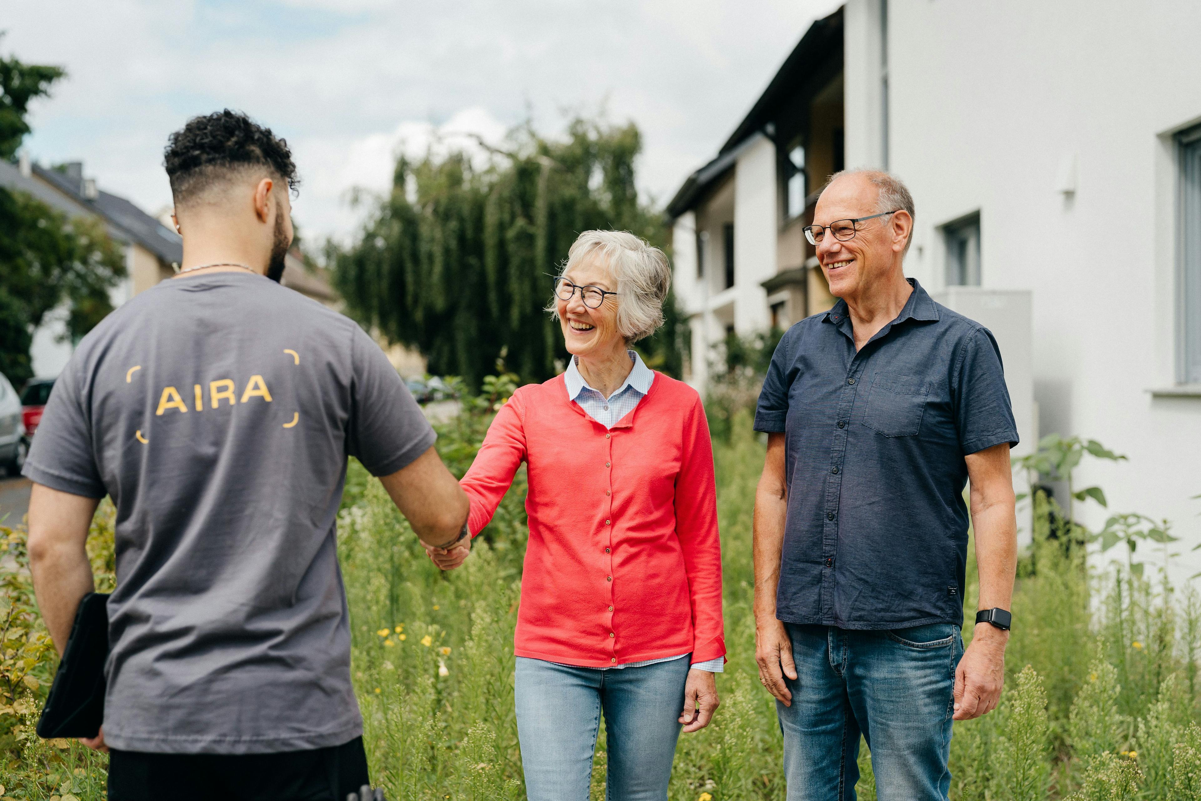 Ein Energie-Berater begrüßt ein älteres Ehepaar vor ihrem Haus