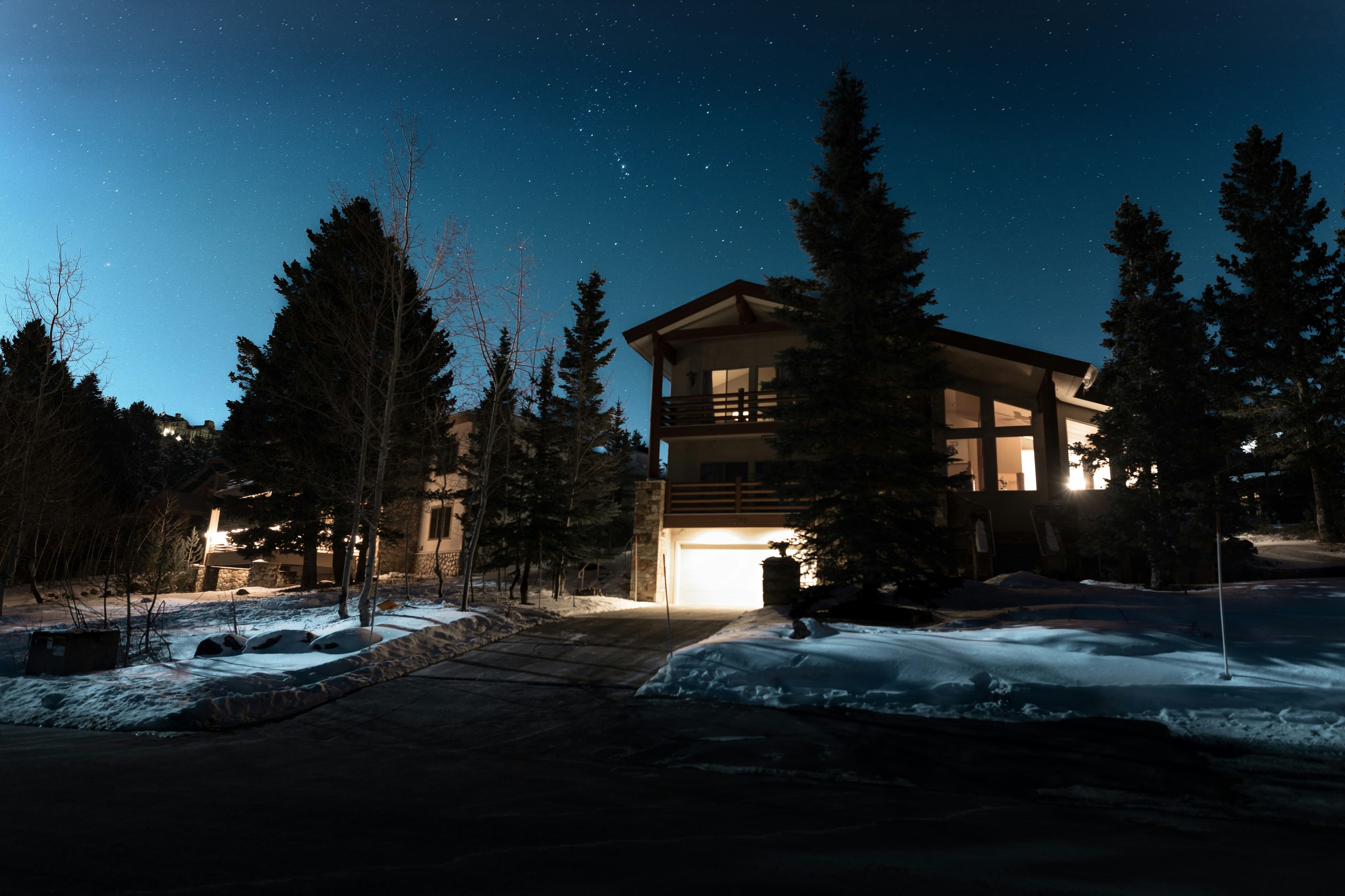 A house partly hidden by some pine trees, with a clear driveway and snow on the ground