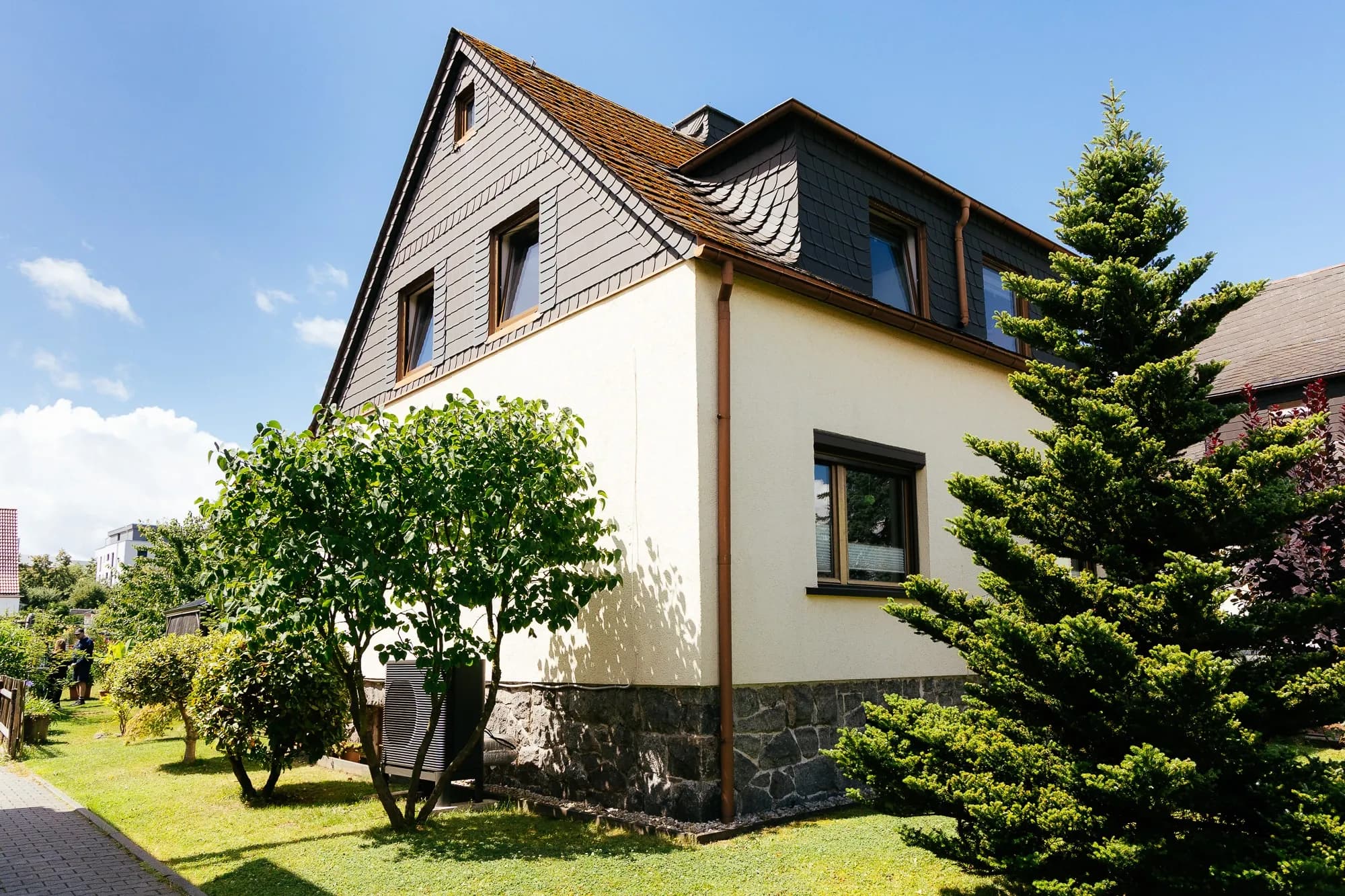 Altbauhaus aus dem Jahr 1918 mit einer Wärmepumpen-Außeneinheit an der Außenwand des Hauses im Garten gestellt