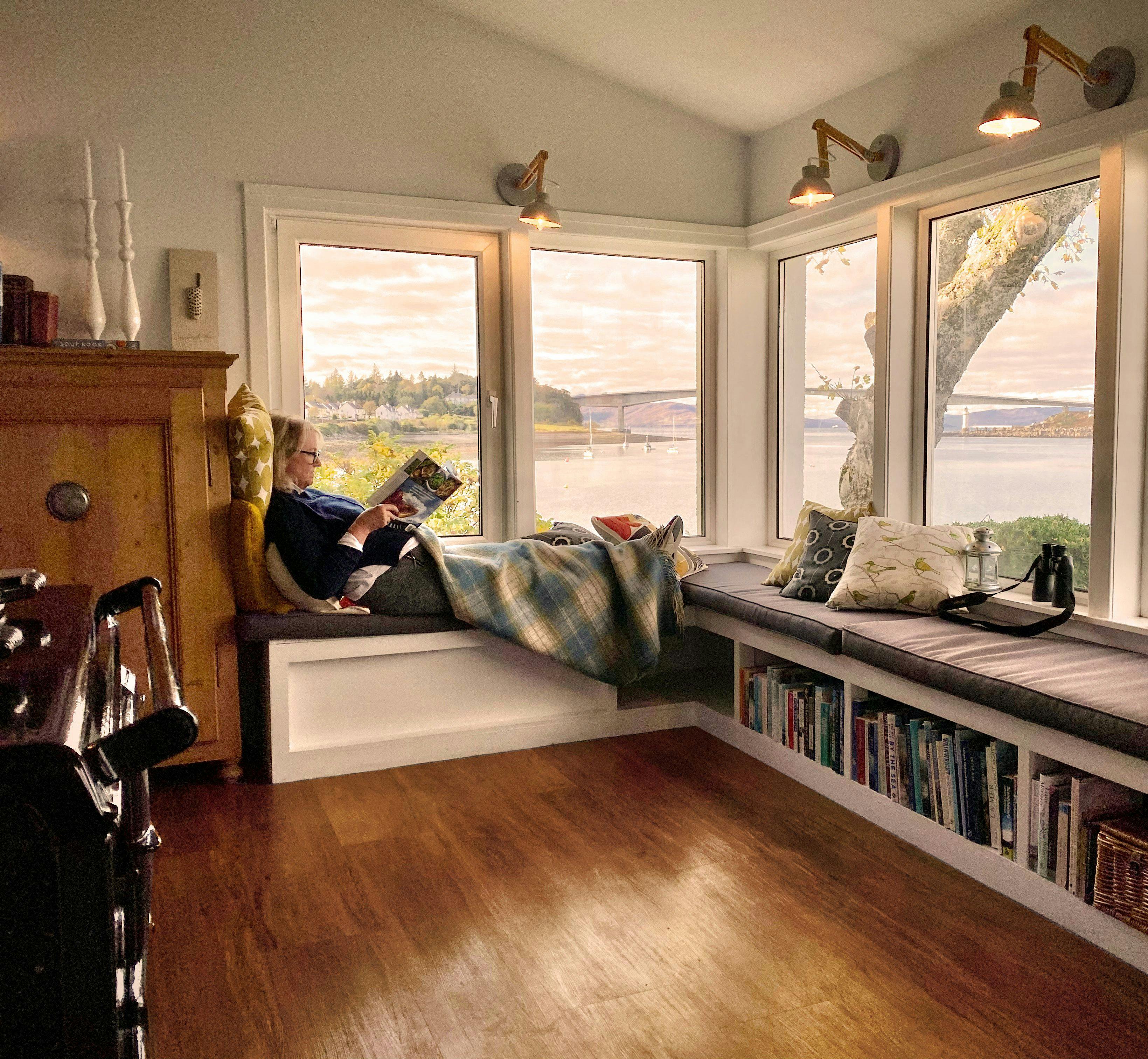 Woman sitting at the window in her home in Scotland reading a magazine