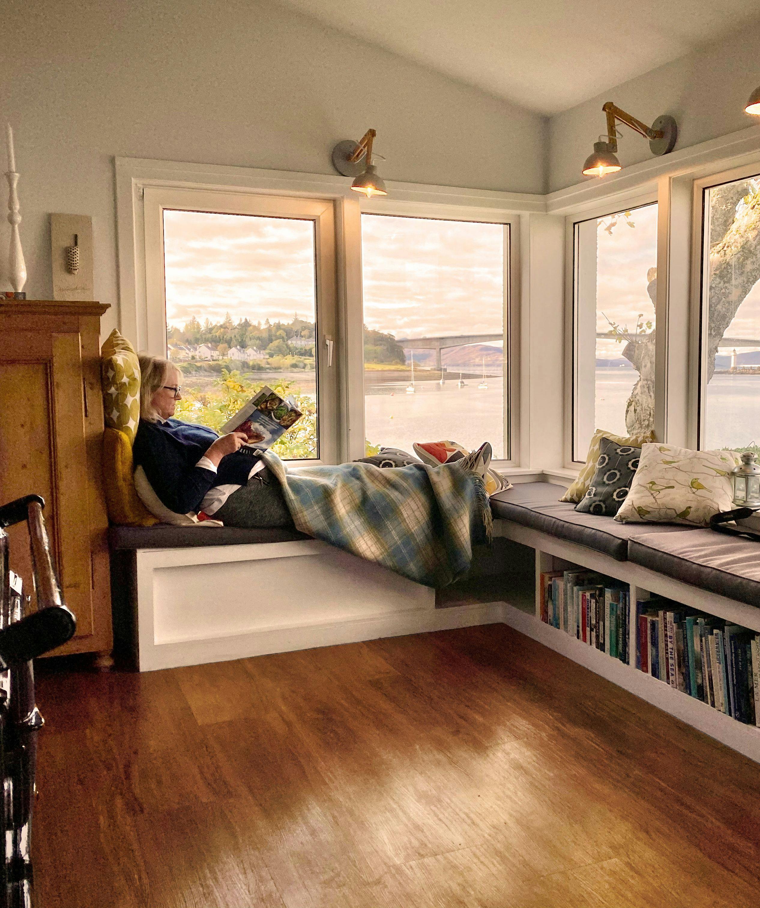 Woman sitting at the window in her home in Scotland reading a magazine 