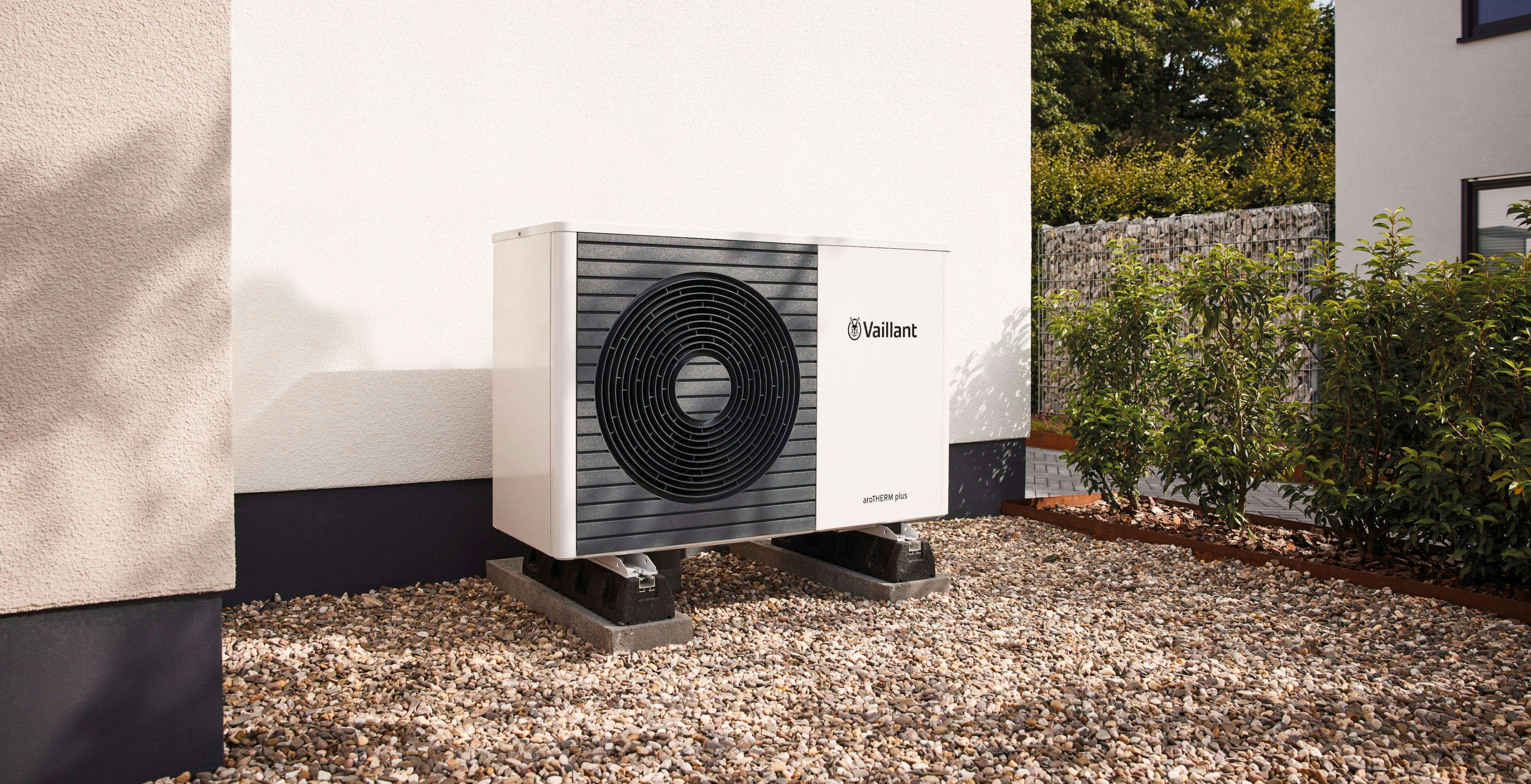 Air to water heat pump against a white wall on some gravel