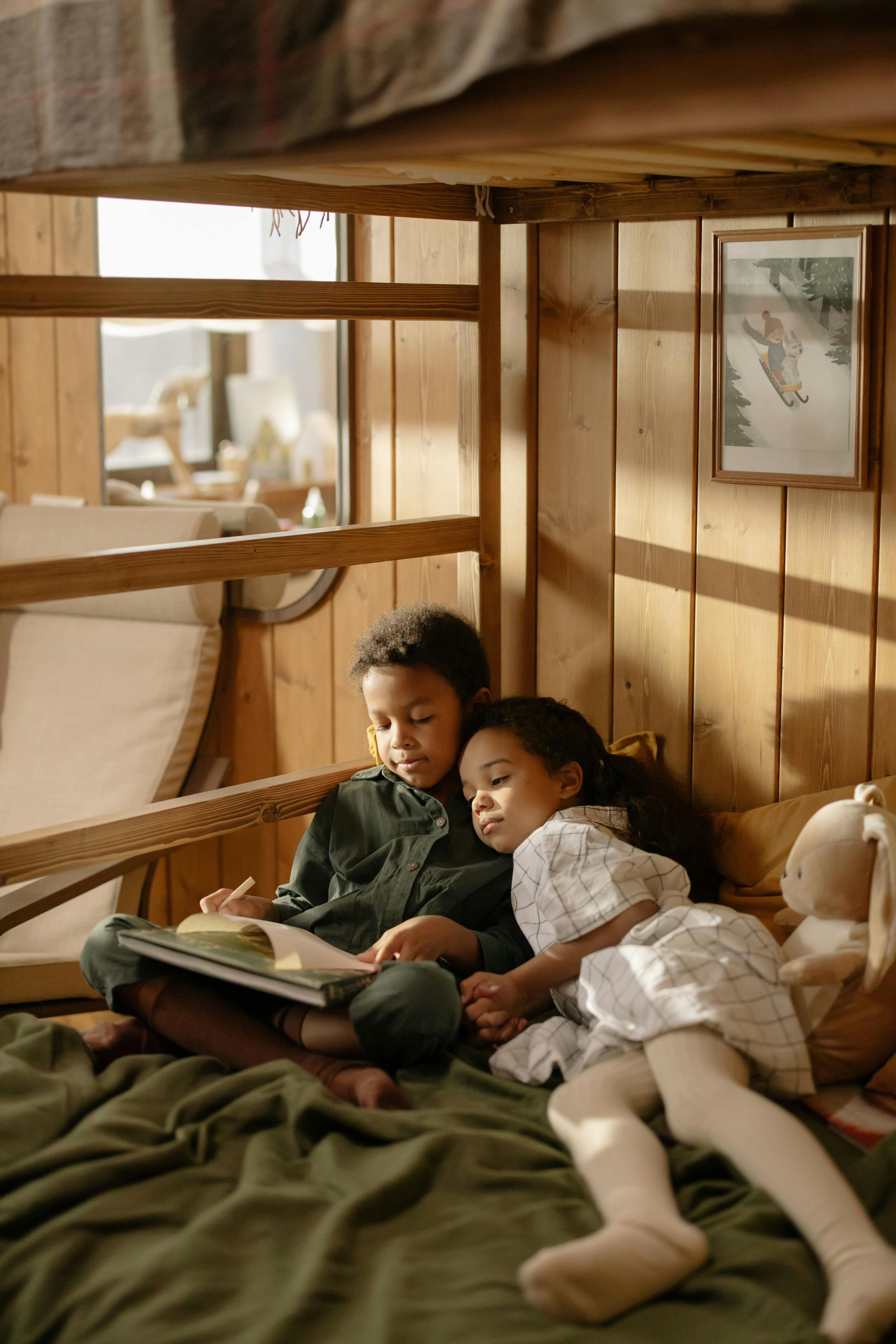 Two children reading a book together in a bunk bed in a room with warm light.