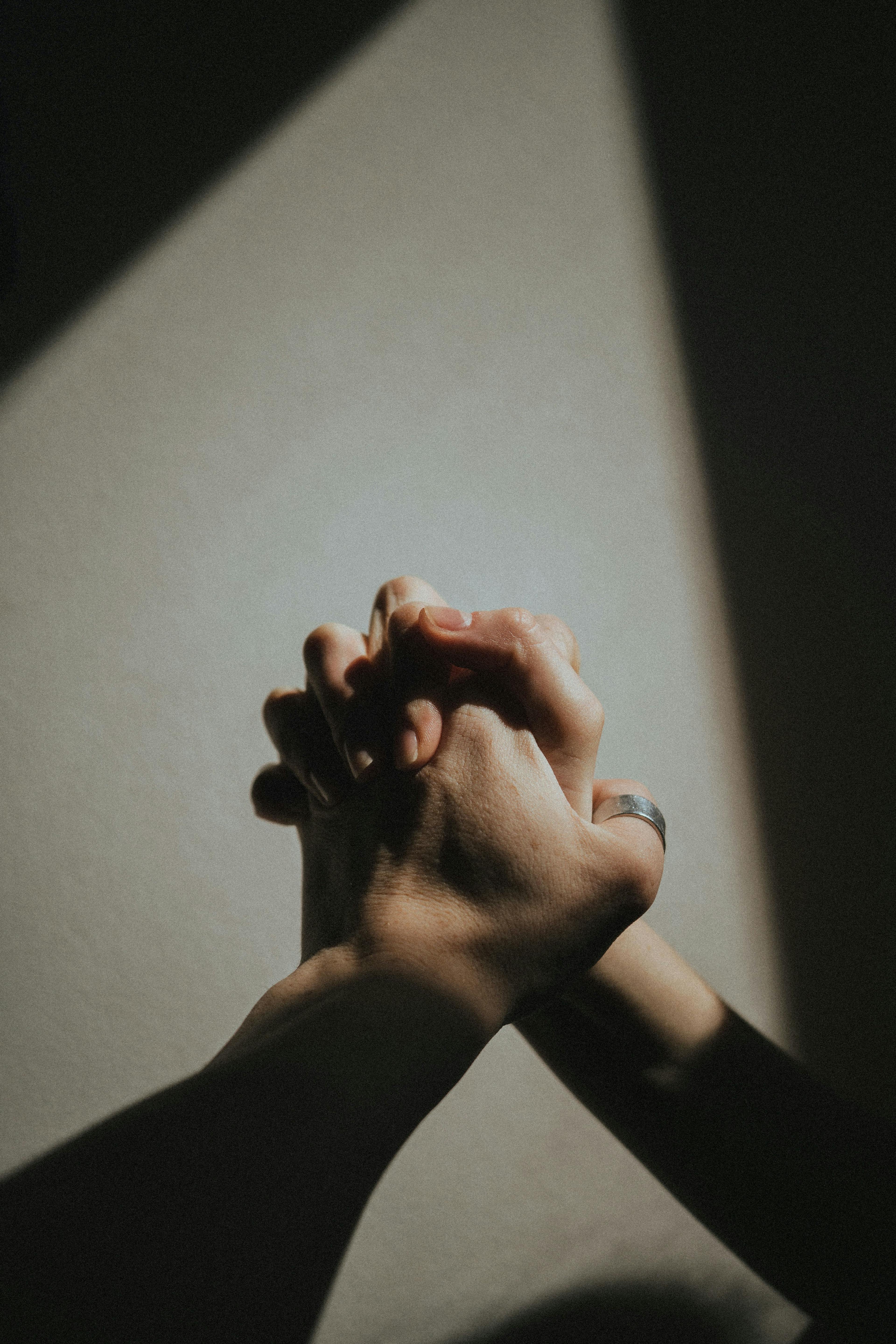 Two hands holding in a dark space with soft light shining upon them.