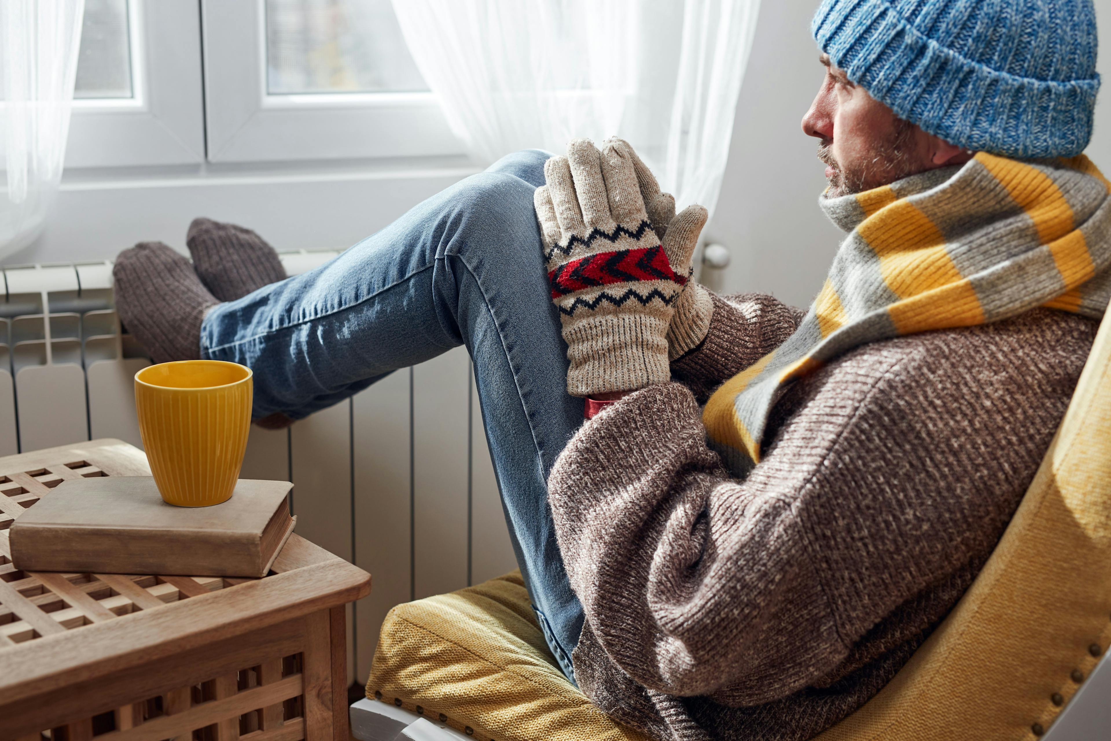 Person sitting by radiator with warm clothes on