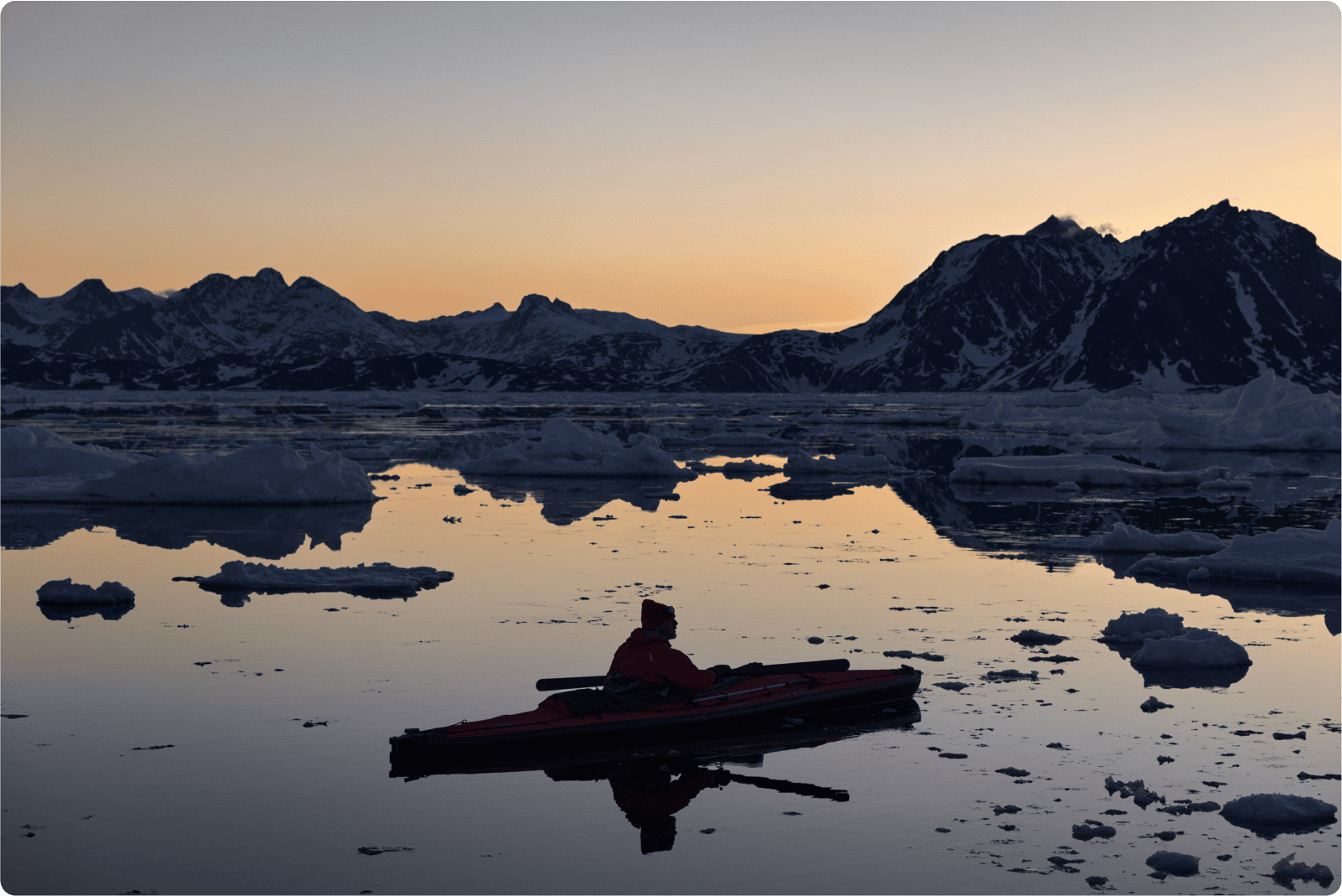 Person kayaking in calm water between blocks of ice at dawn